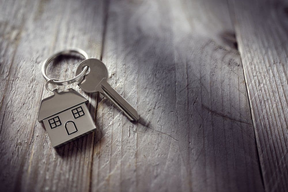 A house key on a ring with a house-shaped keychain, on weathered wood